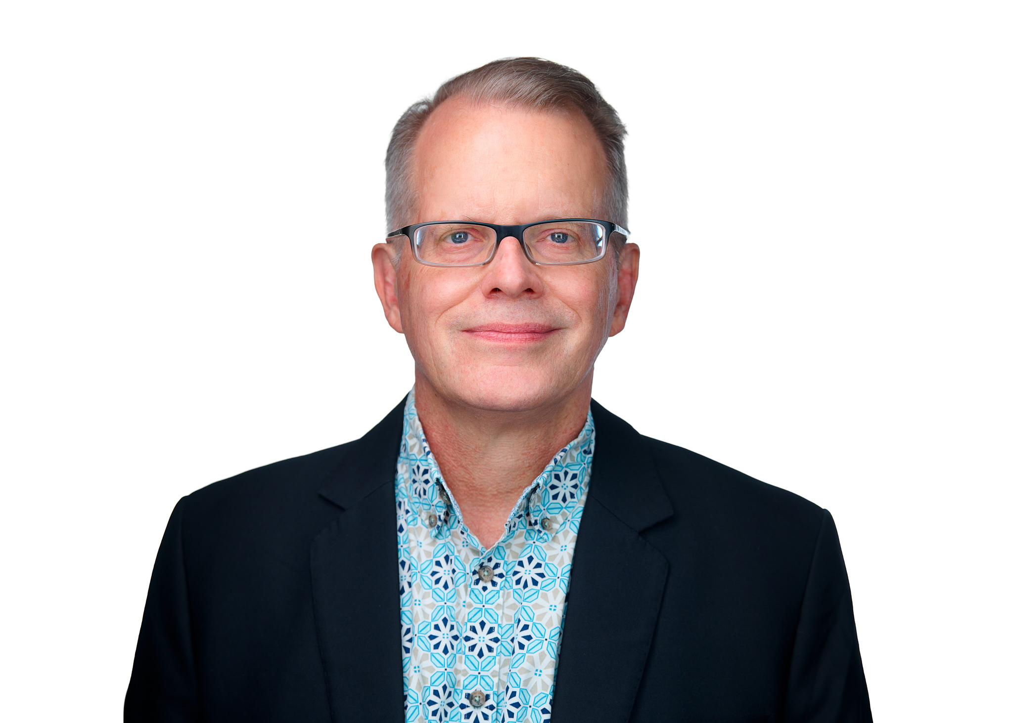 Headshot of a man with short gray hair and glasses, wearing a dark blazer and patterned shirt against a light background